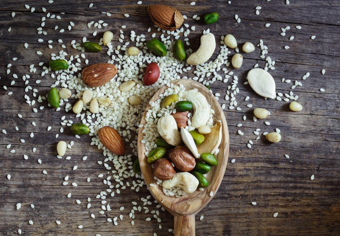 mixed nuts and seeds on wooden spoon over table including pine nuts almonds pistachios and cashews